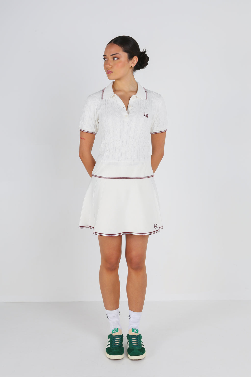 Woman wearing a white PARQ golf outfit with a skirt and shirt on a plain background